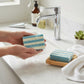 Mellow Monkey Summer Cottage handmade bar soap, blue and white striped, being rinsed under a faucet.