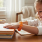 Mellow Monkey Sunburst Orange Feelzies sensory bracelet worn by a young girl reading at a wooden table.