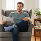 Mellow Monkey Super Dad blue crew socks with superhero design worn by a man reading a newspaper in an armchair