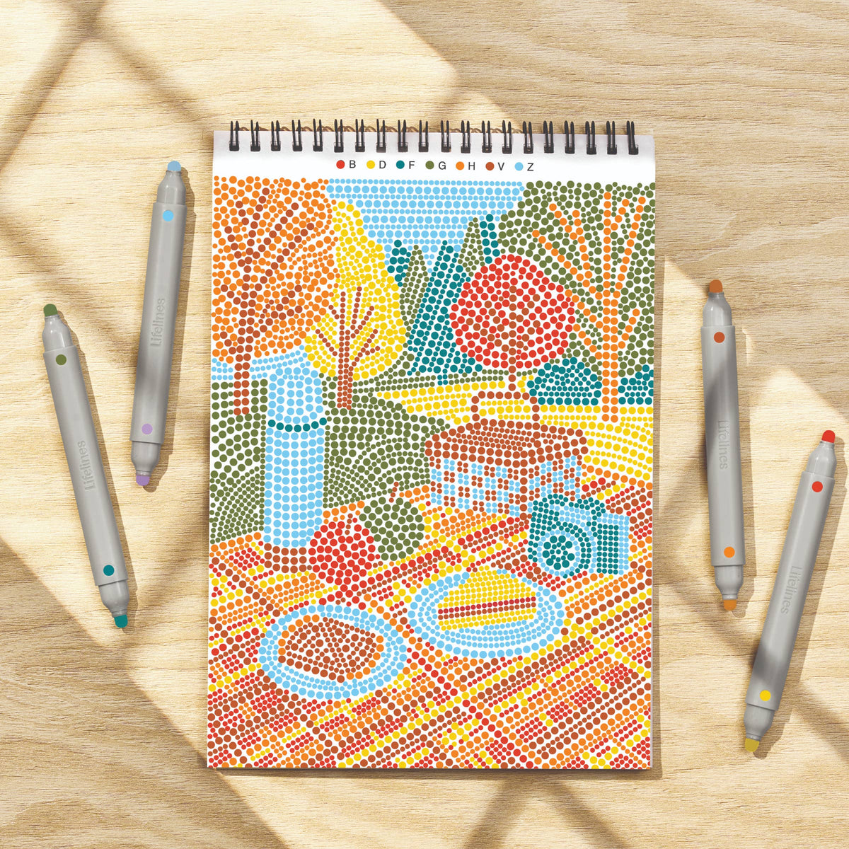 Mellow Monkey Sweater Weather Dot By Letter art pad with four double-sided markers on a wooden table surface.