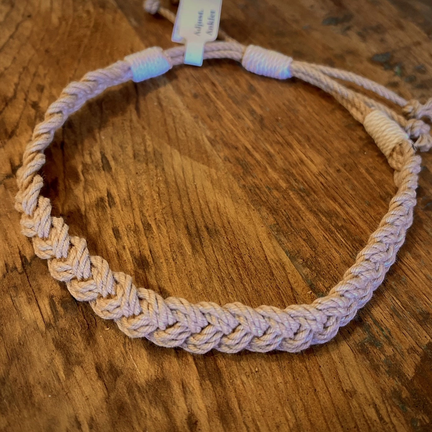 Mellow Monkey tan woven cotton nautical anklet with adjustable sliding knot closure on a wooden surface.