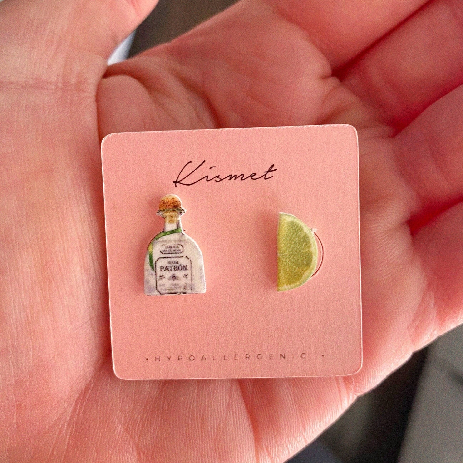 Mellow Monkey handmade tequila bottle and lime wedge stud earrings on a pink display card held in a hand.