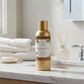 Mellow Monkey Thymes Frasier Fir home fragrance mist in a gold bottle on a marble bathroom vanity with white towels.