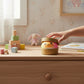 Mellow Monkey tie-dye rainbow dumpling sensory toy with a cute face, held by a child on a wooden nursery desk.