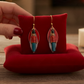 Mellow Monkey handmade layered toy soldier earrings with surgical steel wires displayed on a red velvet cushion.