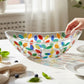 Mellow Monkey Tree of Life Venetian glass oval serving bowl, 13-in, filled with fruit salad. Colorful leaf accents.