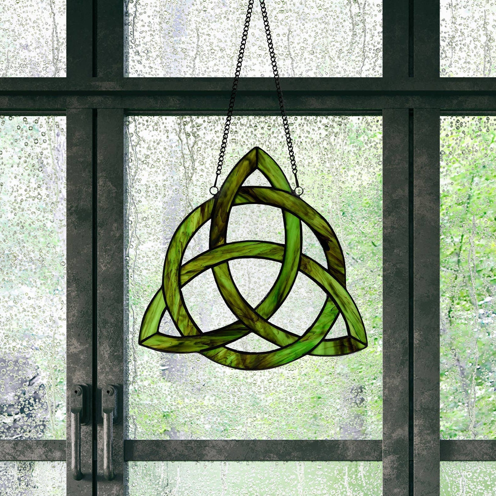 Mellow Monkey Trinity Knot stained glass window panel in emerald green and clear glass hanging in a window.