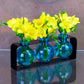 Mellow Monkey Trivo triple aqua recycled glass ball vases in a black metal stand filled with bright yellow flowers.