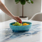 Mellow Monkey turquoise and blue resin oval bowl with base holding fresh fruit on a marble table
