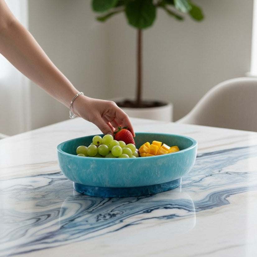 Mellow Monkey turquoise and blue resin oval bowl with base holding fresh fruit on a marble table