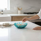 Mellow Monkey handmade turquoise glass coral bowl holding seashells on a white kitchen countertop