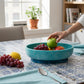 Mellow Monkey turquoise and blue resin oval bowl with base holding fresh fruit on a tiled dining table