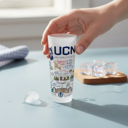 Mellow Monkey Catstudio University of Connecticut 2-oz frosted glass shot glass held by a hand on a blue table