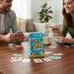 Mellow Monkey UNO Teams card game box on a wooden table with a couple playing in the background