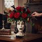 Mellow Monkey Vampira ceramic head vase filled with red roses and black calla lilies on a wooden table.