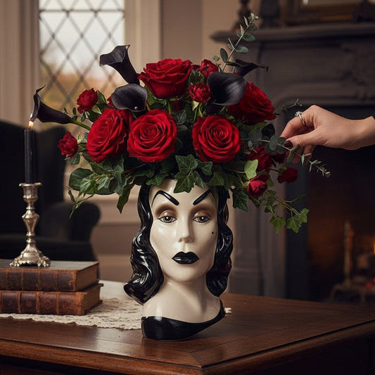 Mellow Monkey Vampira ceramic head vase filled with red roses and black calla lilies on a wooden table.