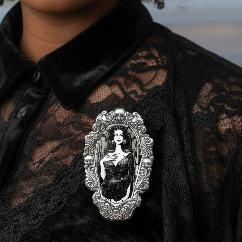 Mellow Monkey Vampira enamel pin in a silver gothic frame, worn on a black lace shirt.
