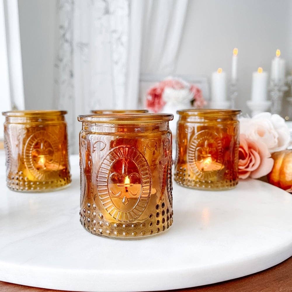 Mellow Monkey set of four vintage amber glass tea light holders with embossed details on a white marble surface.