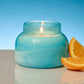 Mellow Monkey Volcano Artisan Signature candle in a turquoise sea glass finish jar with a lit wick. Next to orange slices.