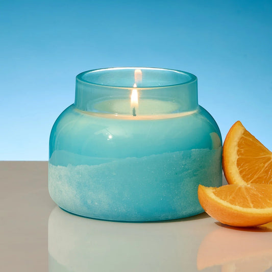 Mellow Monkey Volcano Artisan Signature candle in a turquoise sea glass finish jar with a lit wick. Next to orange slices.