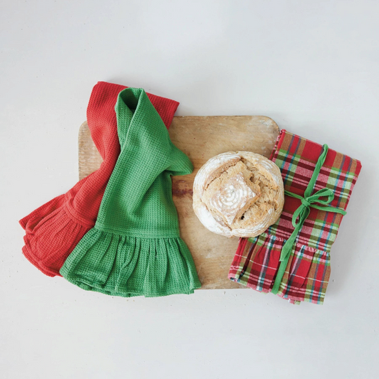 Mellow Monkey set of three waffle weave tea towels with ruffled edges in red, green, and plaid, displayed with bread.
