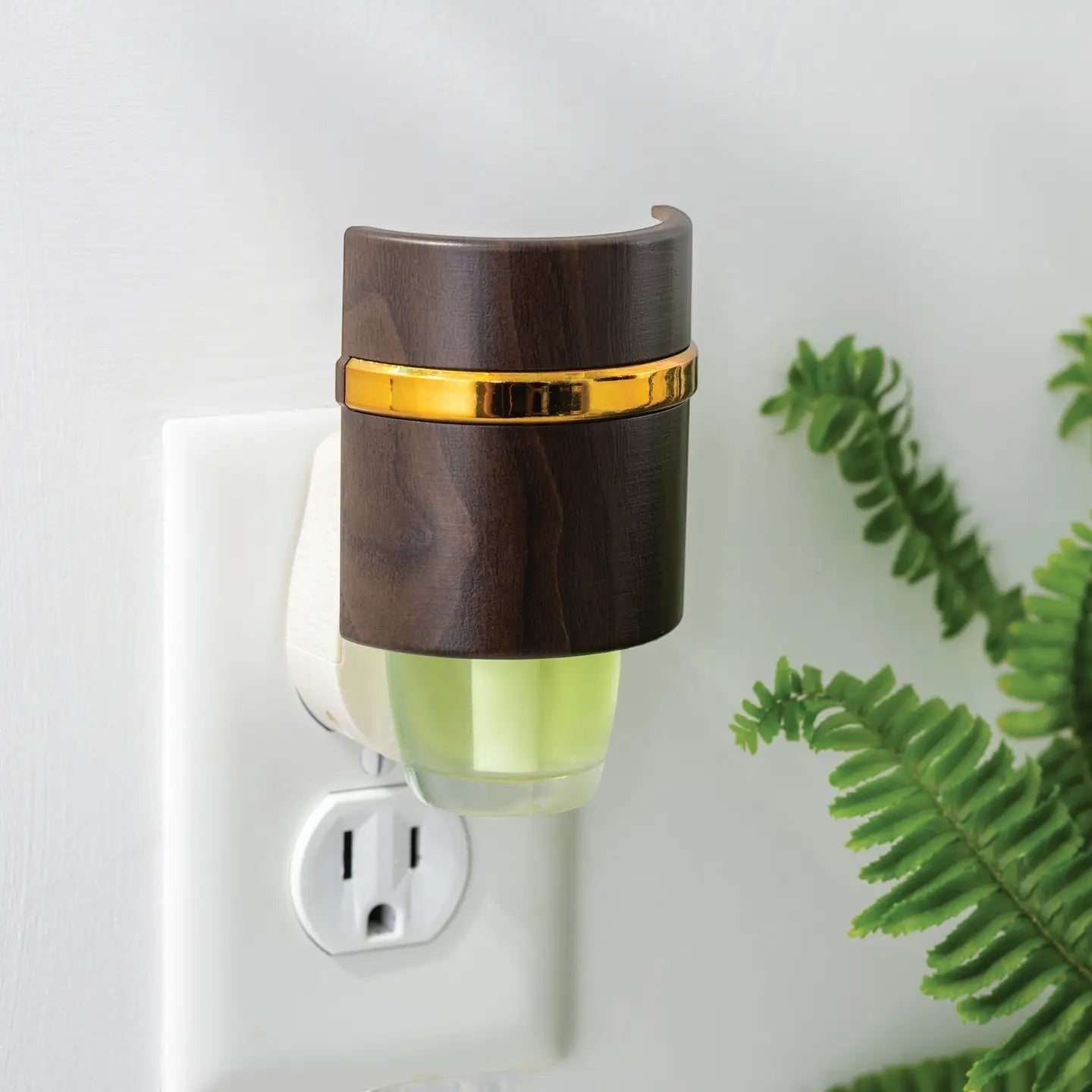 Mellow Monkey Walnut WallScents fragrance warmer with a dark wood finish and gold band plugged into a wall outlet.
