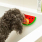 Mellow Monkey Kobe watermelon silicone lick mat with peanut butter, suctioned to a bathtub wall for dog grooming
