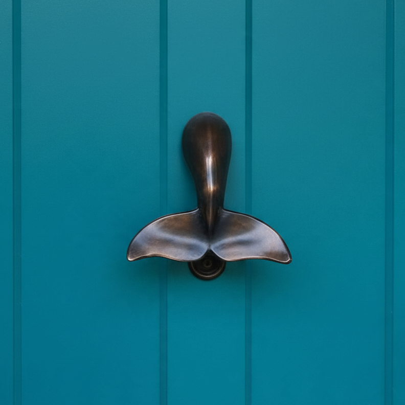 Mellow Monkey whale tail door knocker in oiled bronze mounted on a teal blue door