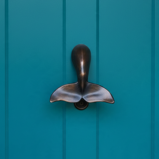 Mellow Monkey whale tail door knocker in oiled bronze mounted on a teal blue door