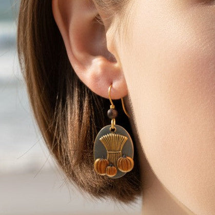 Mellow Monkey Silver Forest autumn earrings featuring wheat and pumpkin charms worn by a woman at the beach