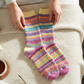 Mellow Monkey Nordic Crew socks featuring a colorful striped pattern on a cozy bed with a book and tea