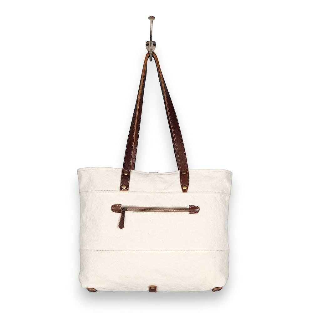 Mellow Monkey white canvas and leather crossbody tote bag with a back zipper pocket hanging on a hook.