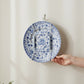Mellow Monkey white wall mount plate hanger holding a decorative blue and white floral ceramic plate on a wall.