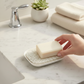 Mellow Monkey white waterfall soap dish with a textured Soap Lift pad holding a bar of soap on a marble countertop.
