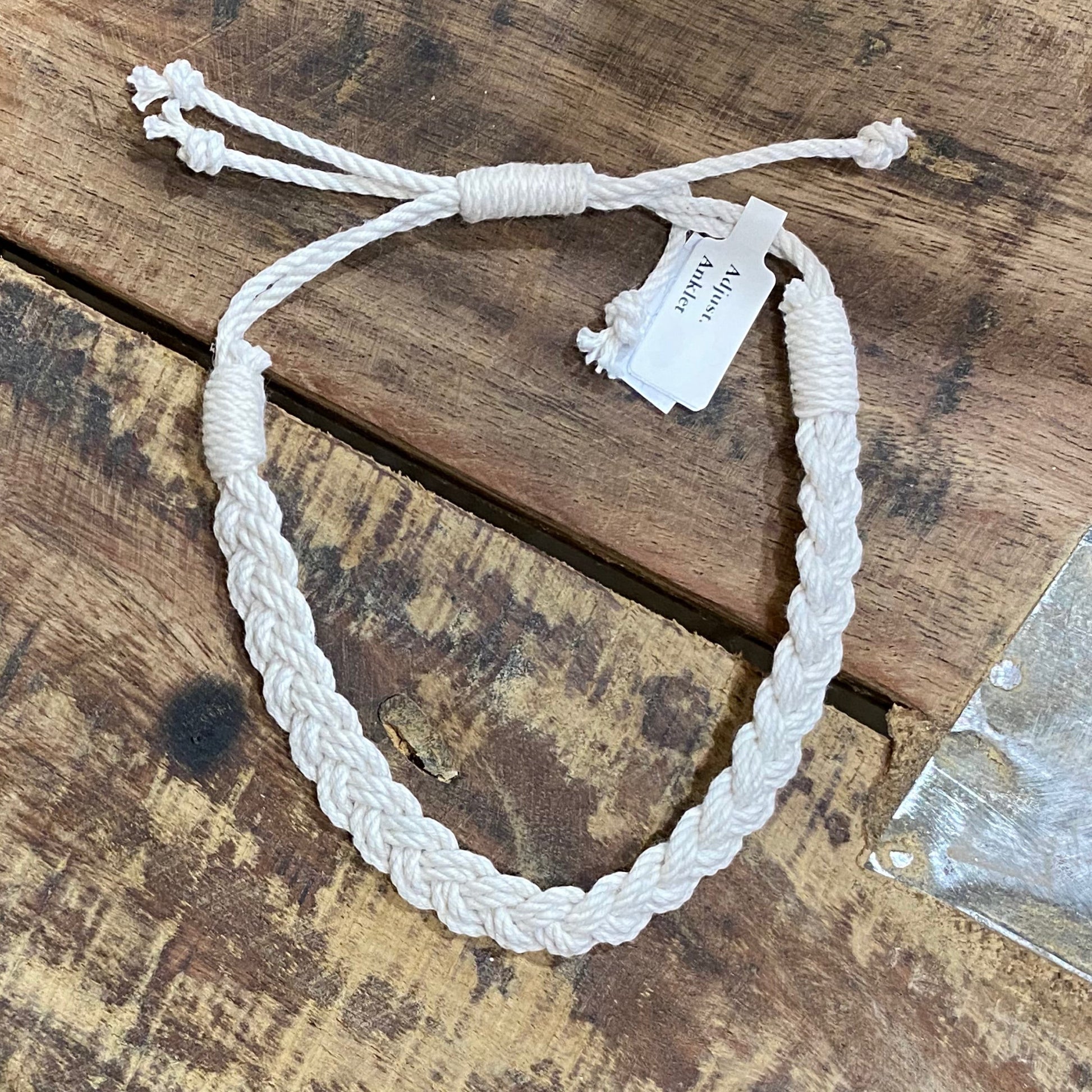 Mellow Monkey white woven cotton nautical anklet with adjustable sliding knot closure on a rustic wood surface.