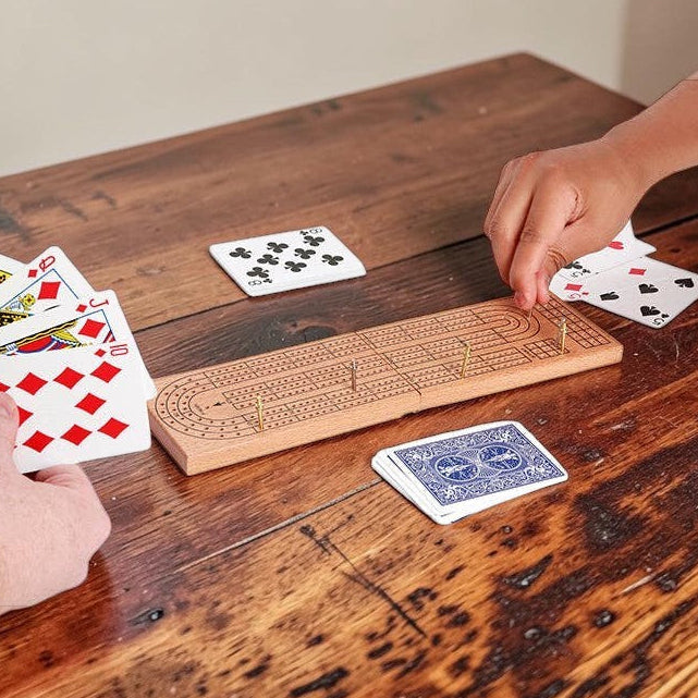 Mellow Monkey wooden cribbage board set with metal pegs and playing cards being used by two players