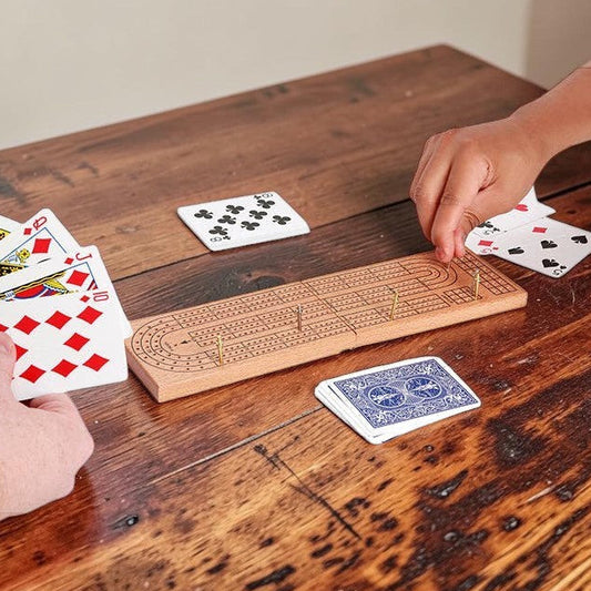 Mellow Monkey wooden cribbage board set with metal pegs and playing cards being used by two players