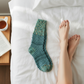 Mellow Monkey Woodland crew sock in teal and brown textured knit pattern resting on white bed sheets