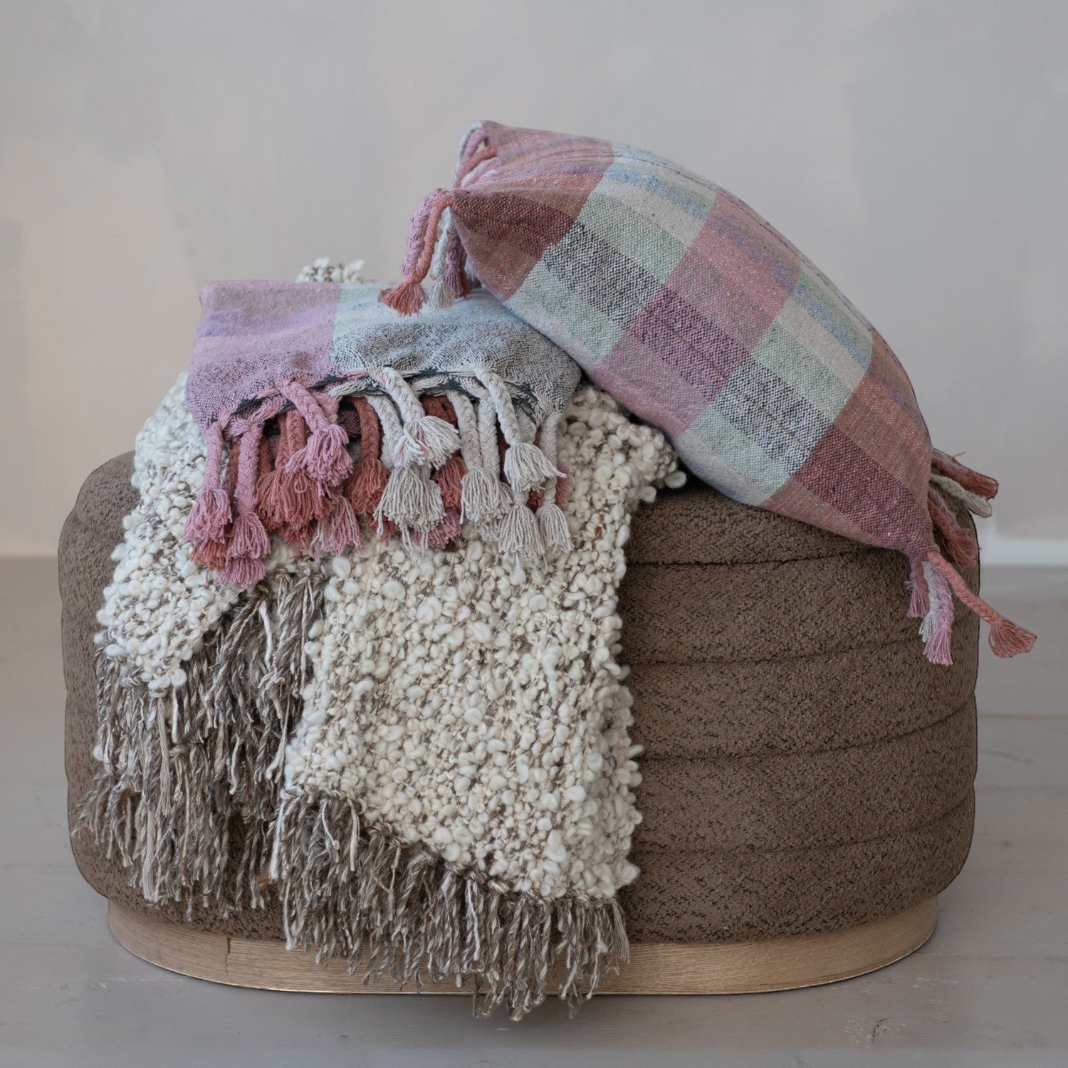 Mellow Monkey woven wool blend throw blanket in cream with fringe and a pink and blue plaid bolster pillow.