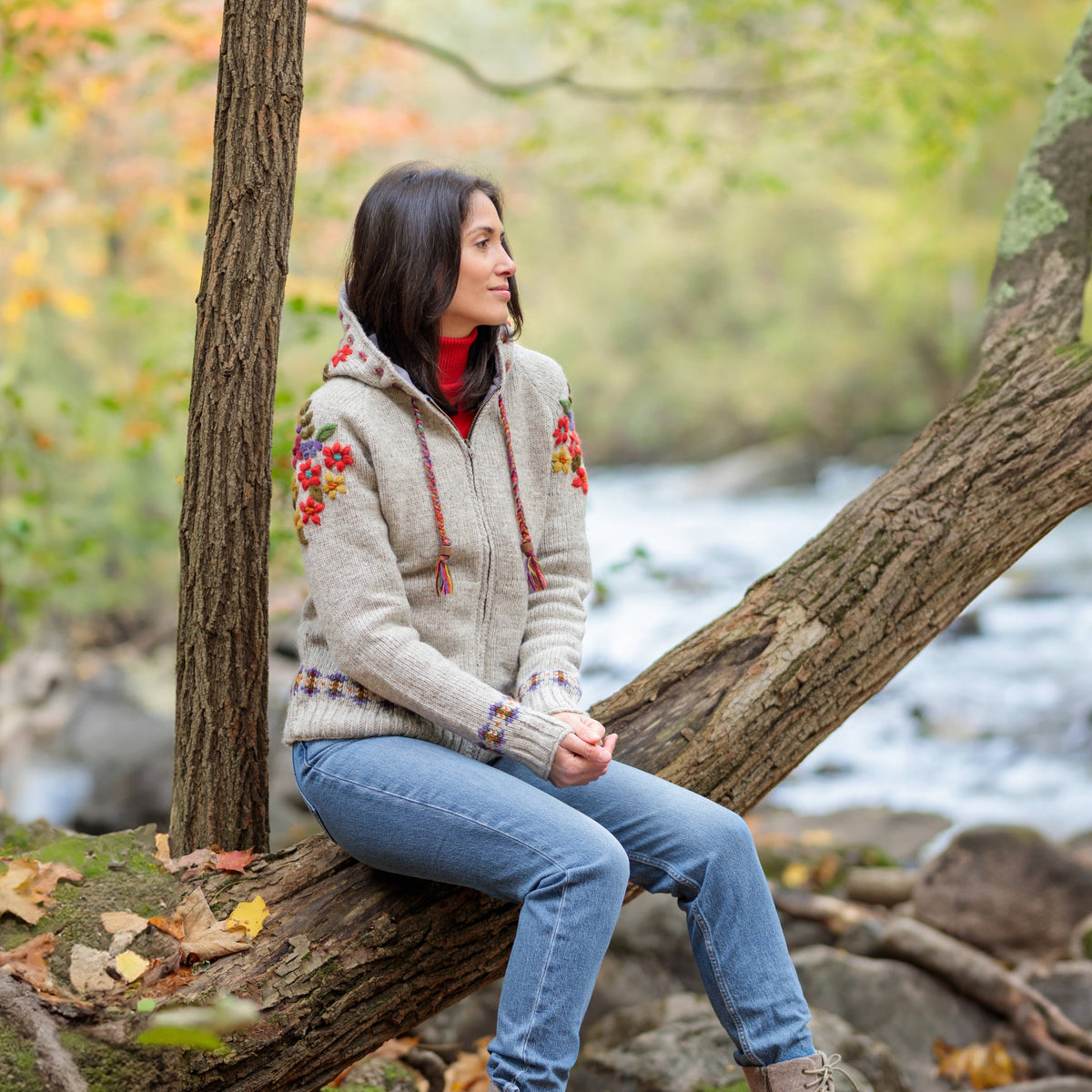 Mellow Monkey light natural wool zip hoodie with colorful floral embroidery, worn by a woman sitting on a tree log.