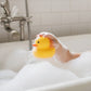 A happy child playing with a Mellow Monkey yellow rubber duck in a bubble-filled bathtub.