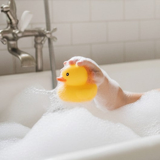 A happy child playing with a Mellow Monkey yellow rubber duck in a bubble-filled bathtub.