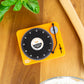 Mellow Monkey retro vinyl record shaped kitchen timer in bright yellow on a wooden countertop with fresh basil