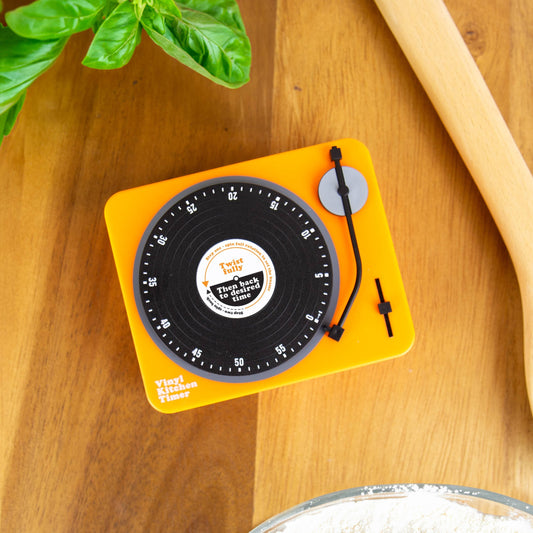 Mellow Monkey retro vinyl record shaped kitchen timer in bright yellow on a wooden countertop with fresh basil