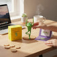 Mellow Monkey Yoga Frog figurine in tree pose with mini book and yellow gift box on a wooden desk