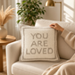 Mellow Monkey square decorative pillow with gray punch-embroidered You Are Loved text on a cream textured fabric