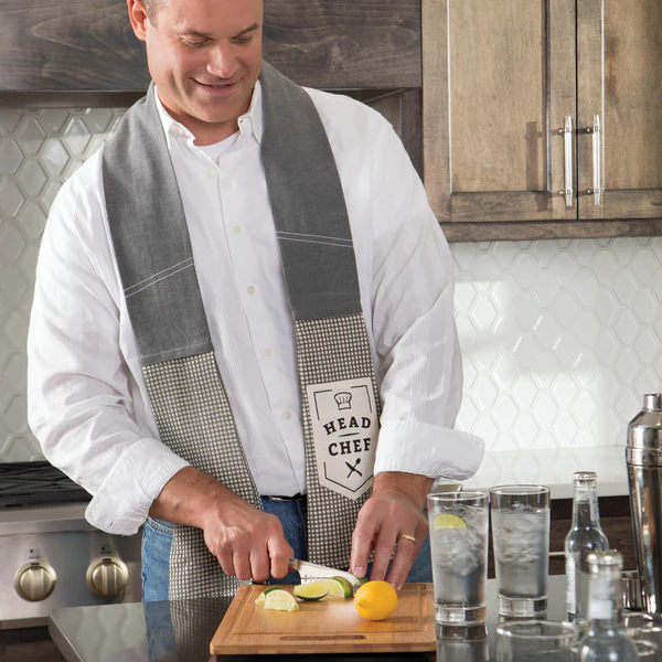 Caucasian middle aged man cutting fruit in kitchen wearing a gray kitchen boa that reads, Head Chef 