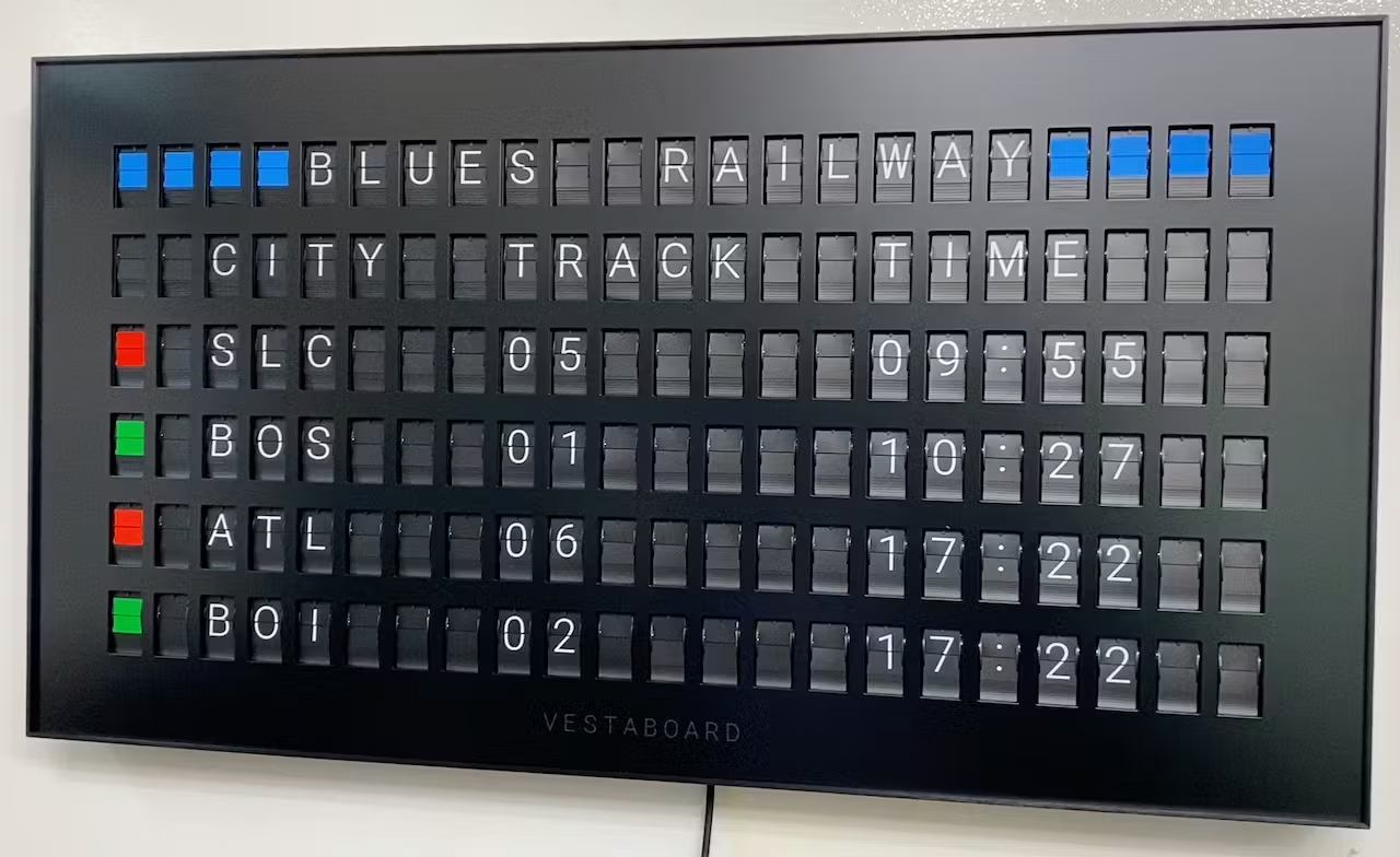 Vestaboard example display. white split flap letters on black background example display of a railway schedule showing four train departures, track number and times