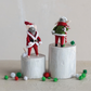 Mellow Monkey handmade wool felt mouse ornaments in red and green holiday outfits standing on wooden pedestals.