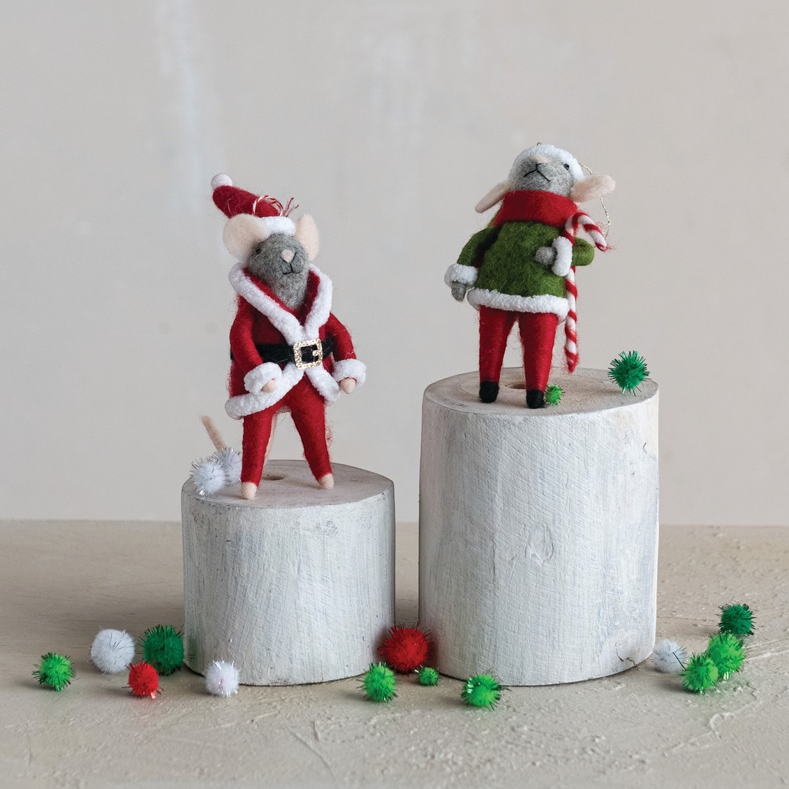 Mellow Monkey handmade wool felt mouse ornaments in red and green holiday outfits standing on wooden pedestals.